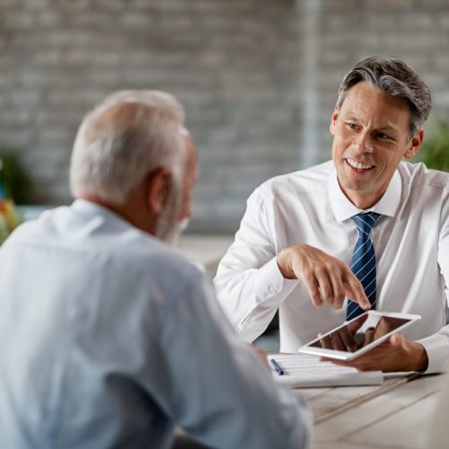 Happy bank manager using touchpad while talking with senior clients on a meeting in the office.